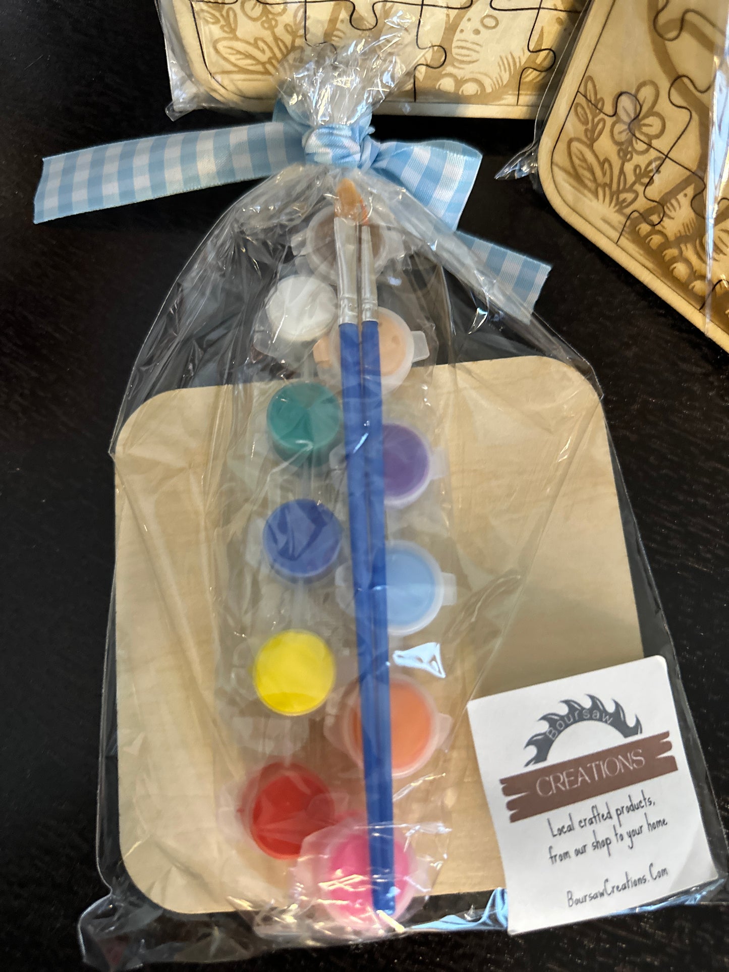 Shows back of puzzle with included 12 watercolor paints with a brush in package tied with a ribbon.