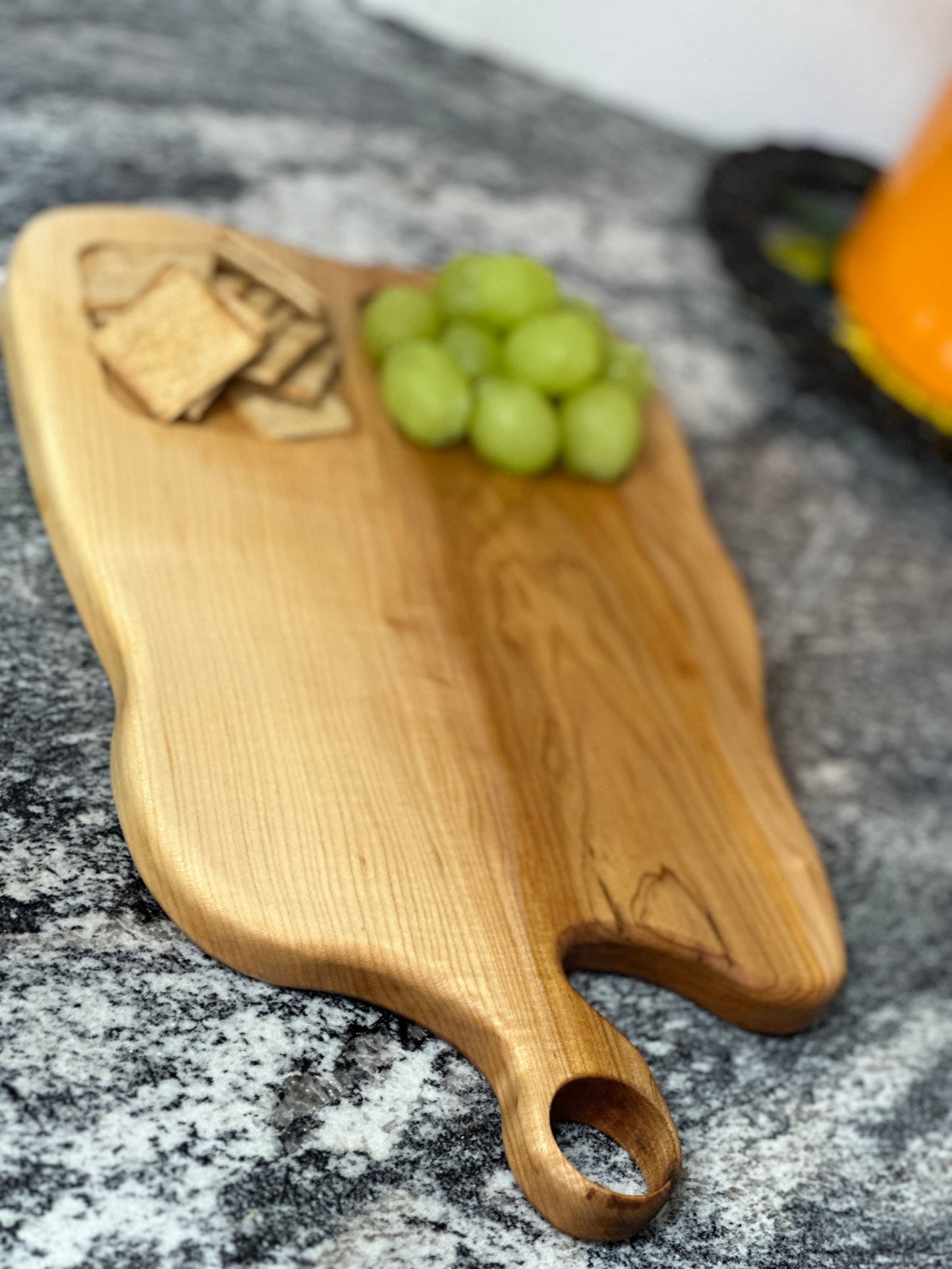 Maple light wood charcuterie board with food sections filled with grapes and crackers