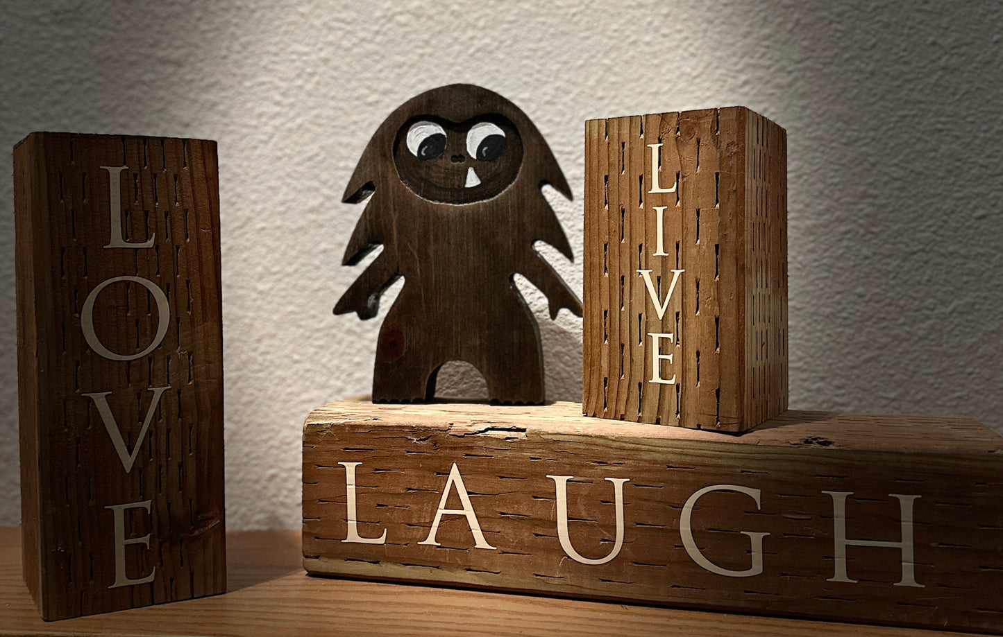 Hardwood Large Bigfoot in blue pine and walnut stain with smiling one-tooth mouth, set on 3 wood blocks with Live, Love, Laugh painted on them