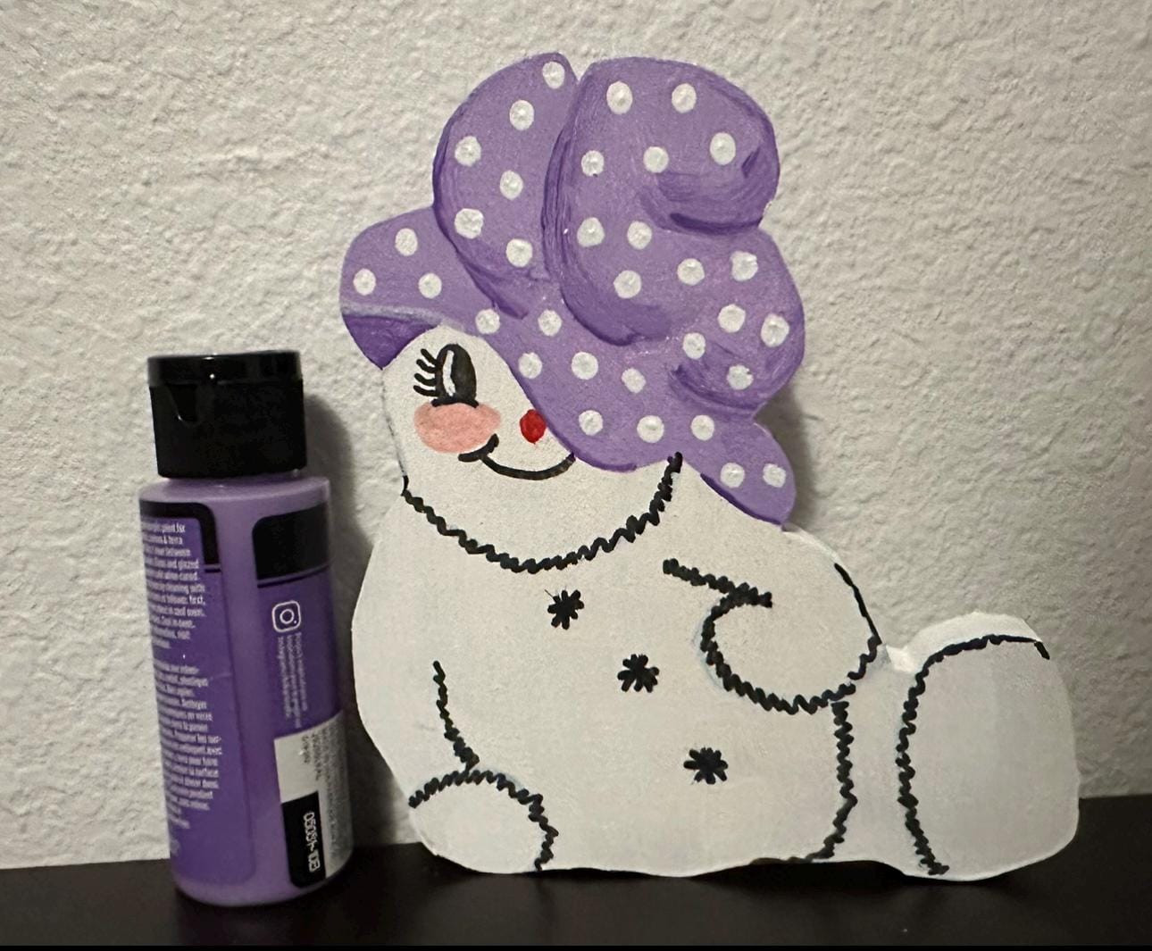 Wood painted snow woman shelf sitter with purple painted cap sitting next to 2oz paint bottle