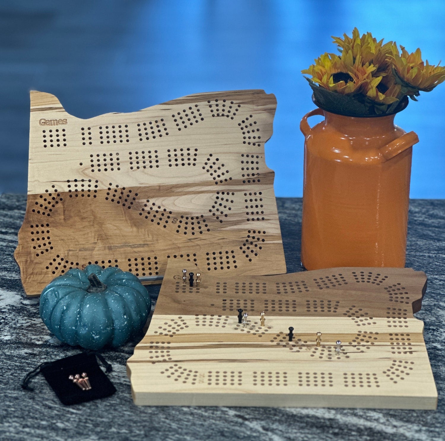 Two cribbage boards, one stood up and the other laying flat with decorative flowers next to them.