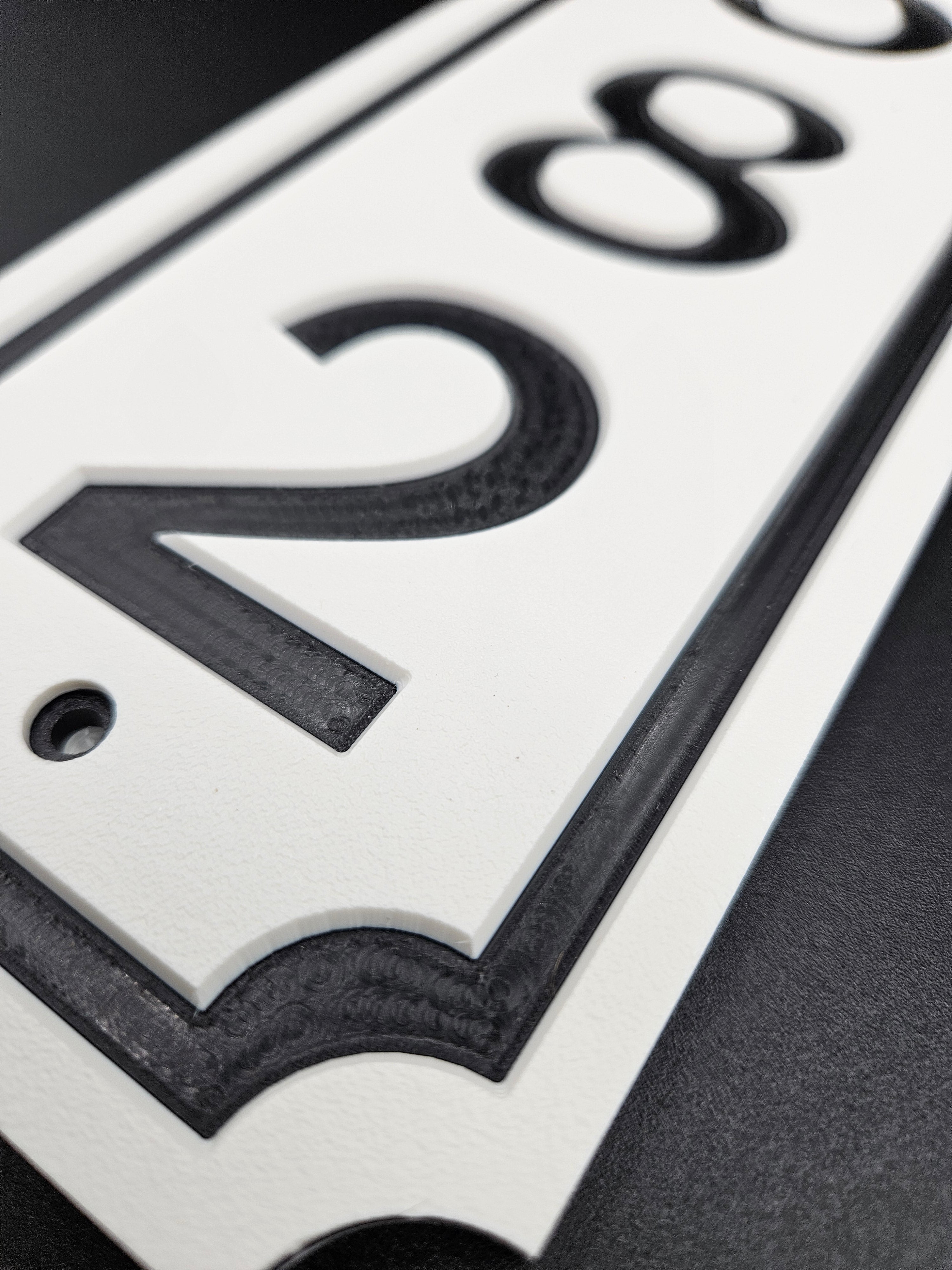Close-up of carved white and black HDPE vertical address sign showing machining, border and corner detail