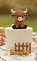 Table setting with a cake featuring a highland cow 3d printed figurine, Sheep party favors bears, and decorative birthday elements outdoors.