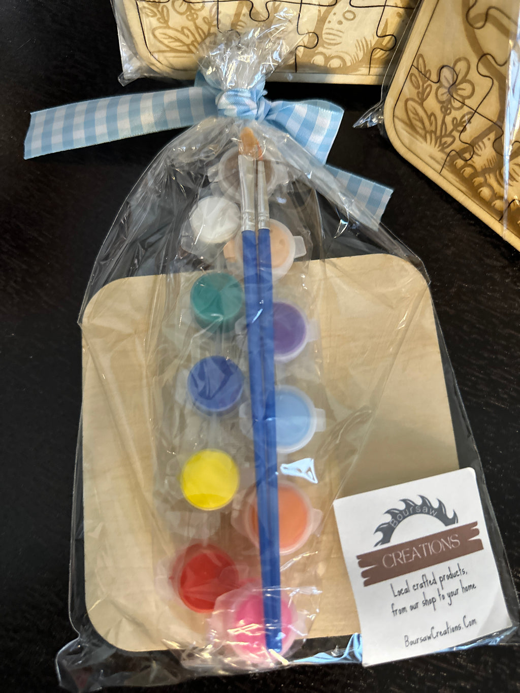 Shows back of puzzle with included 12 watercolor paints with a brush in package tied with a ribbon.