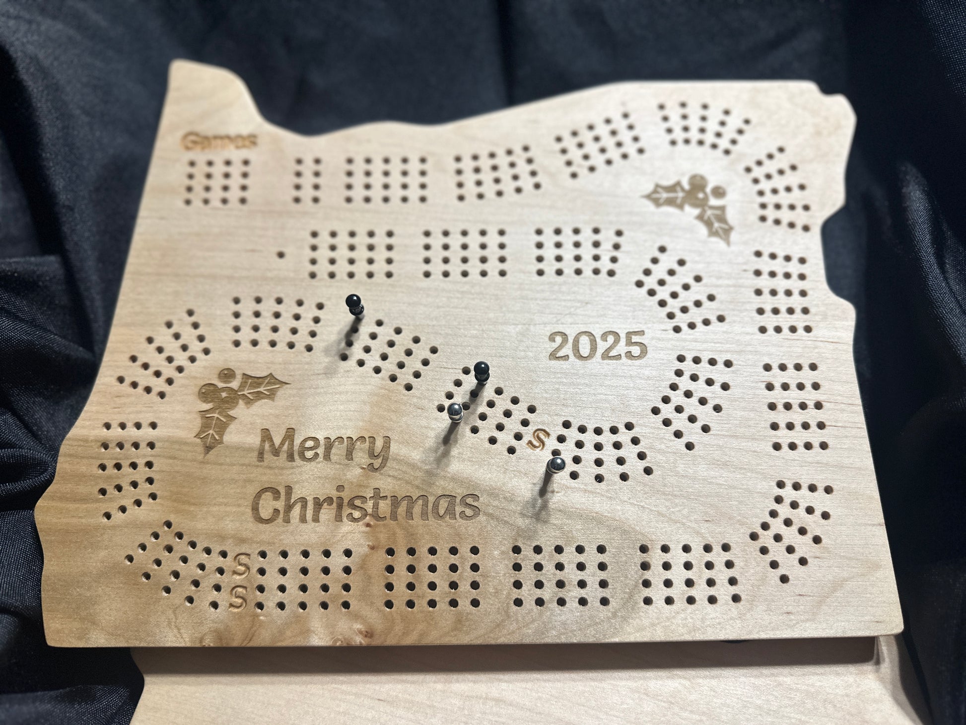 Oregon calico maple Christmas cribbage board with 'Merry Christmas' and '2025' engraved, on a dark background
