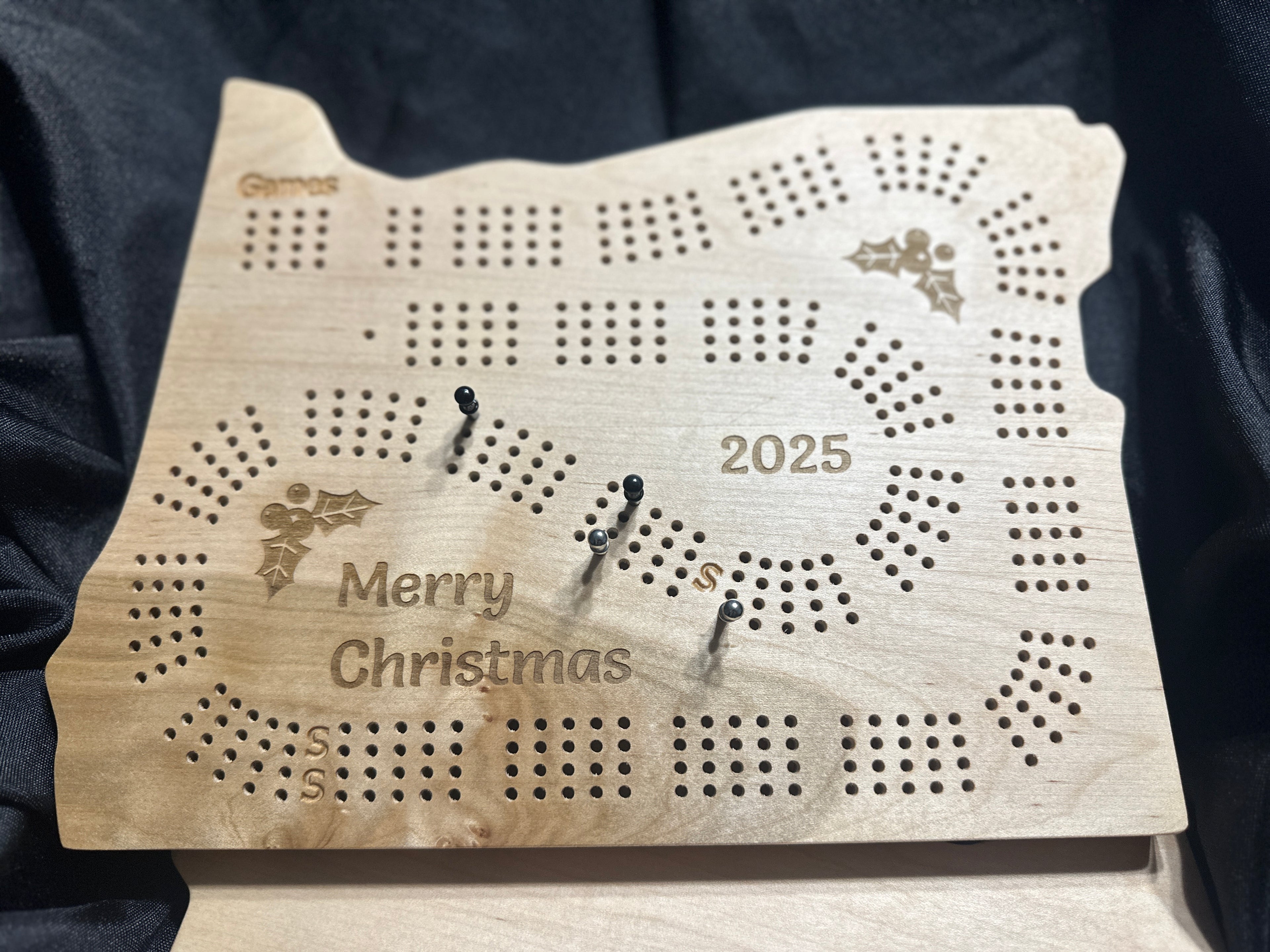 Oregon calico maple Christmas cribbage board with 'Merry Christmas' and '2025' engraved, on a dark background
