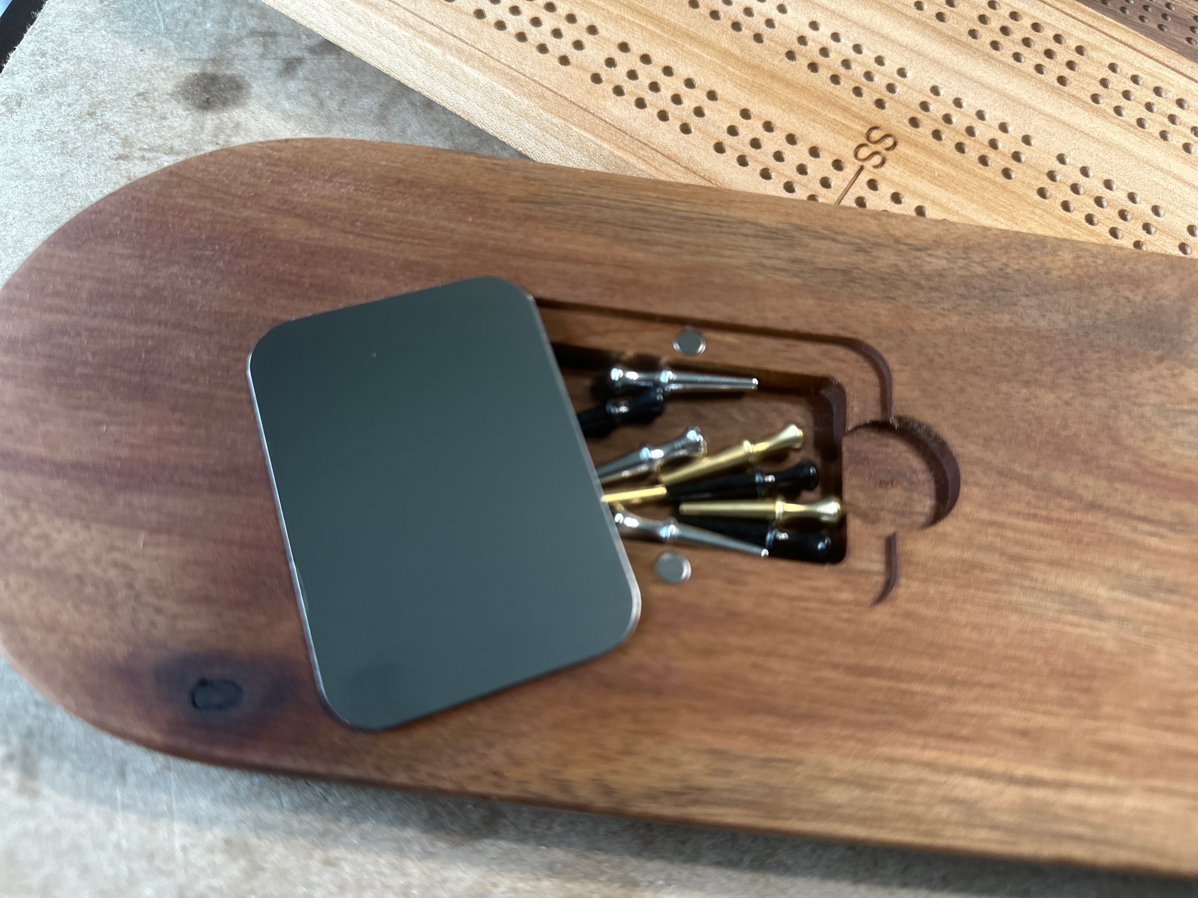 Small cutout box with metal cover and magnet holes on back of cribbage board with gold, black and silver metal pegs