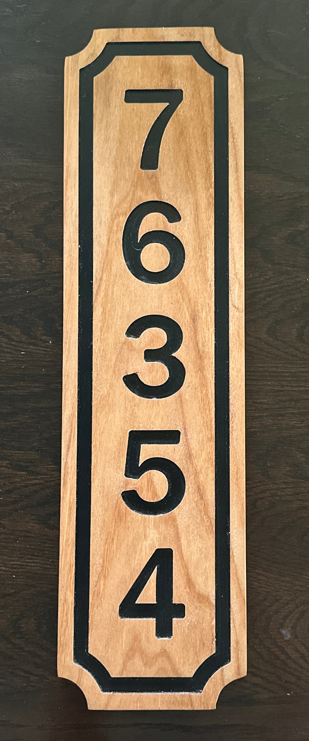 Vertical wooden address plaque with black numbers on a dark background