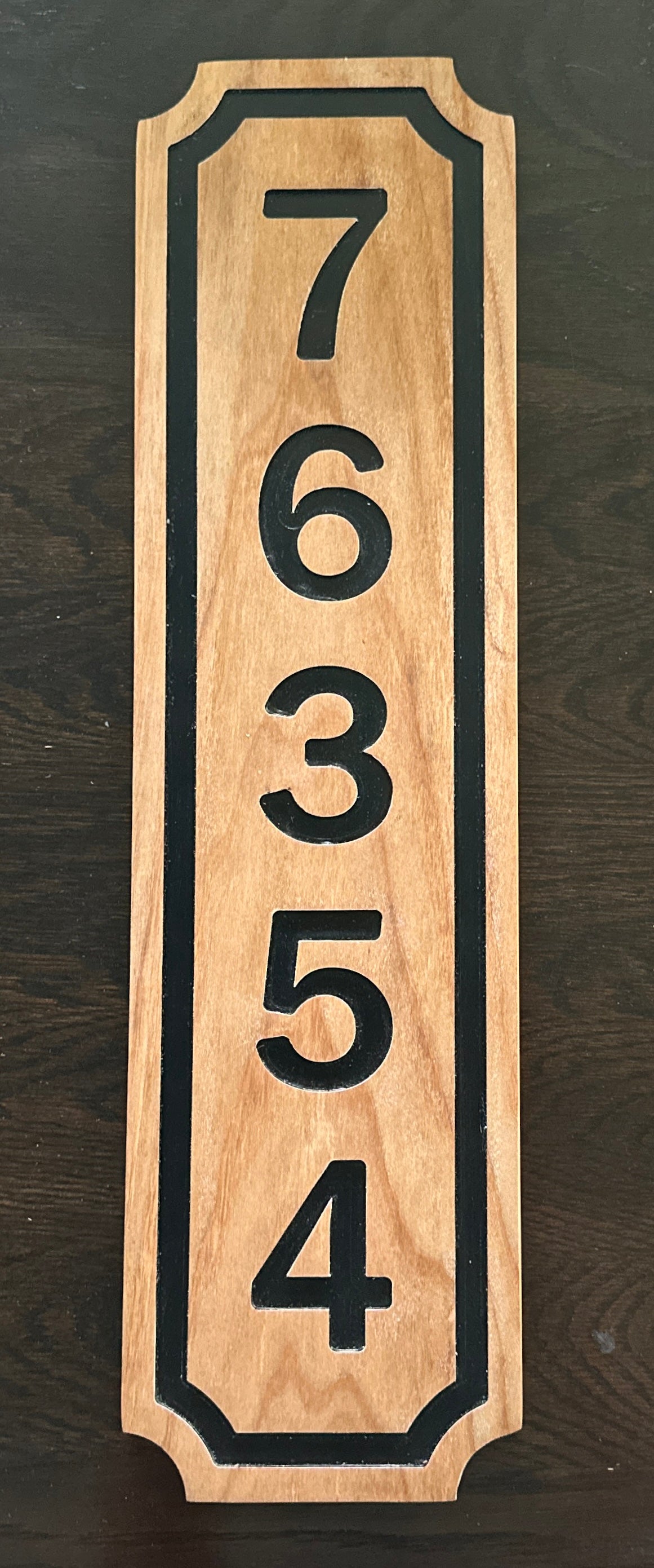 Vertical wooden address plaque with black numbers on a dark background