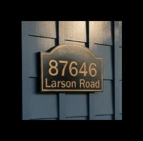 House exterior with a blue shingle wall and wooden door, featuring a custom house number sign.