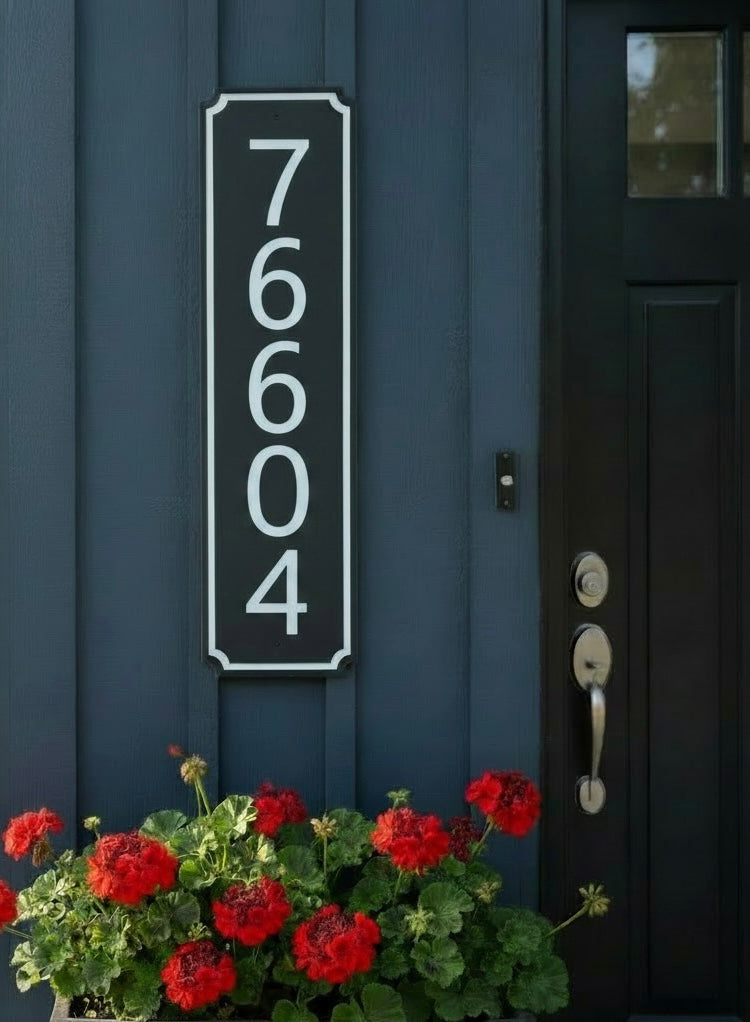 Vertical black and white address sign  on a blue house with a flower pot in front.
