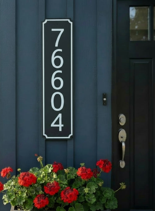 Vertical black and white address sign  on a blue house with a flower pot in front.