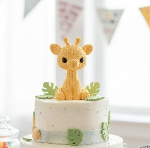 Small cake with a 3d printed "knitted" style giraffe on top in a indoor party setting