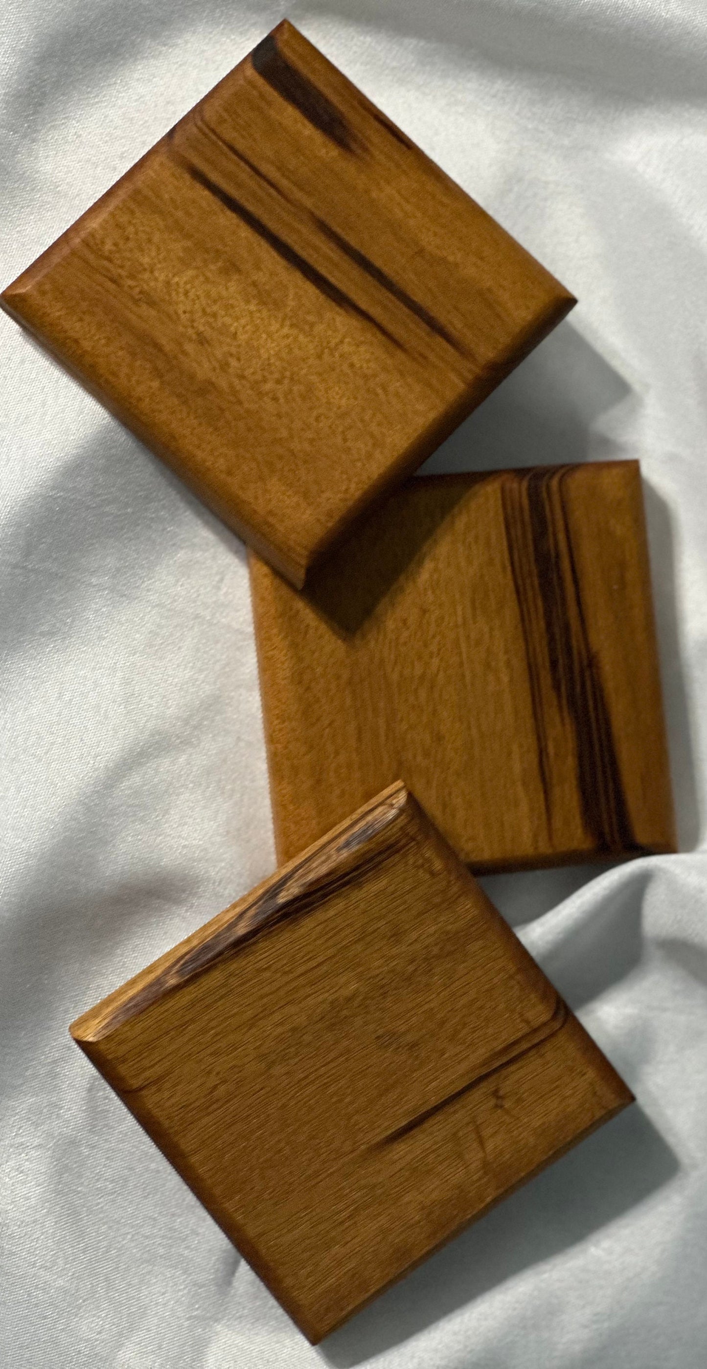 Three Brazil wood coasters displayed one leaning on the other in a cascading fashion on white linen.