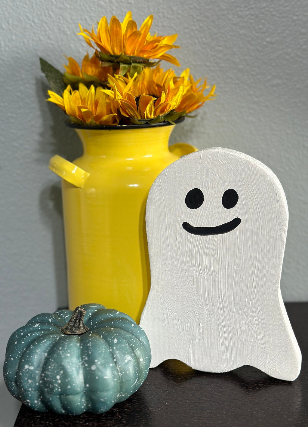 wooden ghost with smile by yellow milk can vase with sunflowers and pumpkin