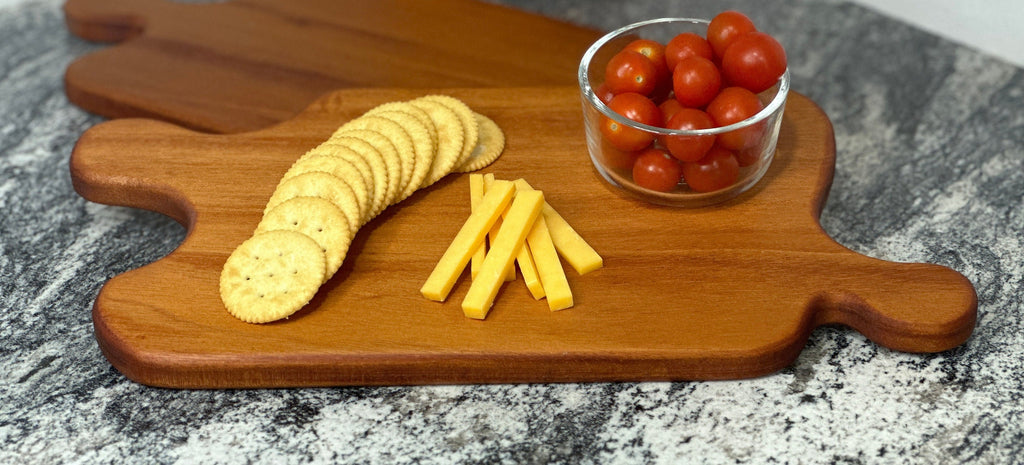 Mahogany red hardwood jigsaw puzzle shaped charcuterie board with cherry tomato, cheese and crackers displayed on a black and white countertop