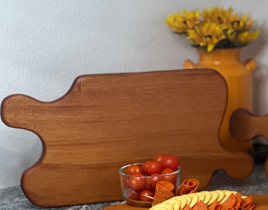 Mahogany red hardwood jigsaw puzzle shaped charcuterie board with cherry tomato, meat and crackers displayed in front of an orange milk can vase with sunflowers