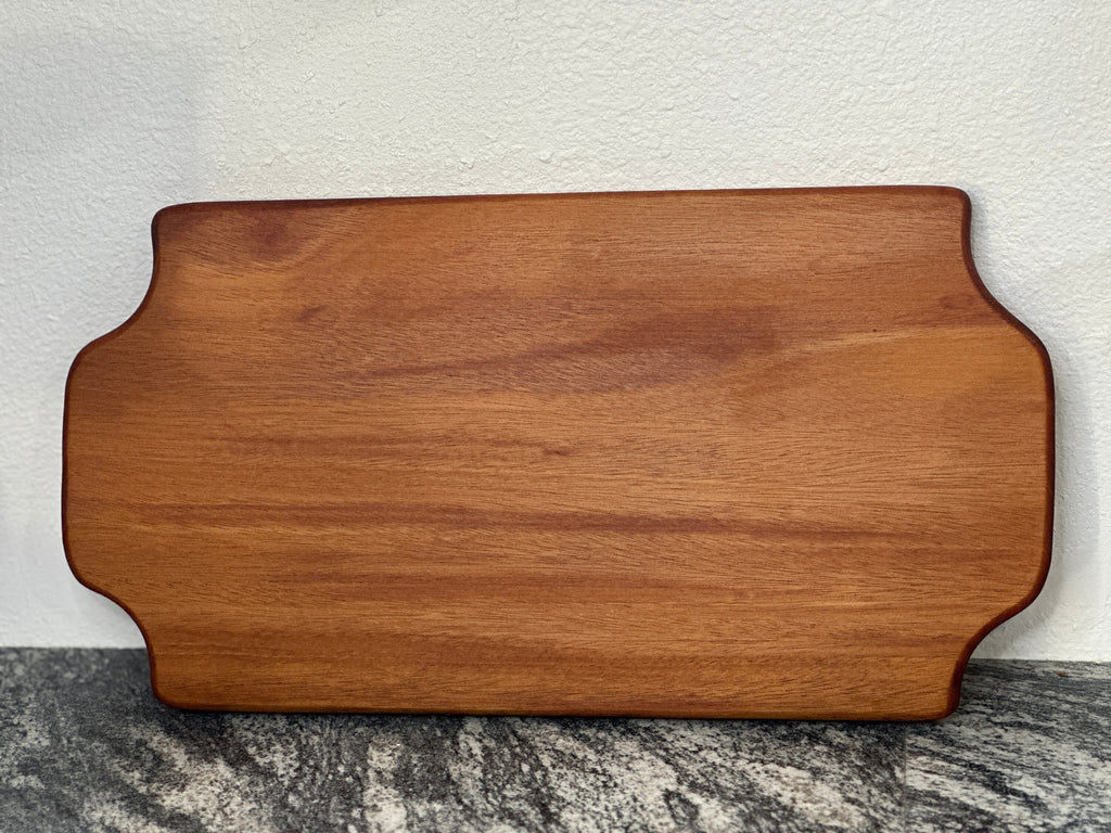 Mahogany red hardwood tray style charcuterie board leaning against white wall on a black and white countertop
