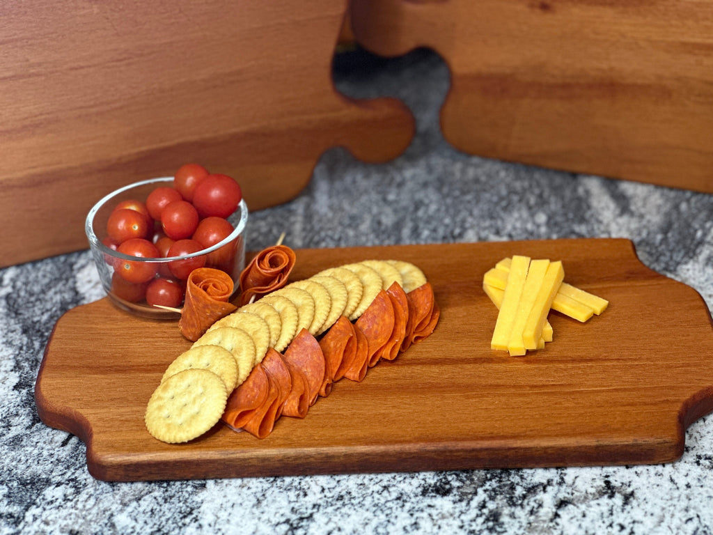Mahogany red hardwood tray style charcuterie boards with cherry tomato, meat, cheese and crackers displayed in front