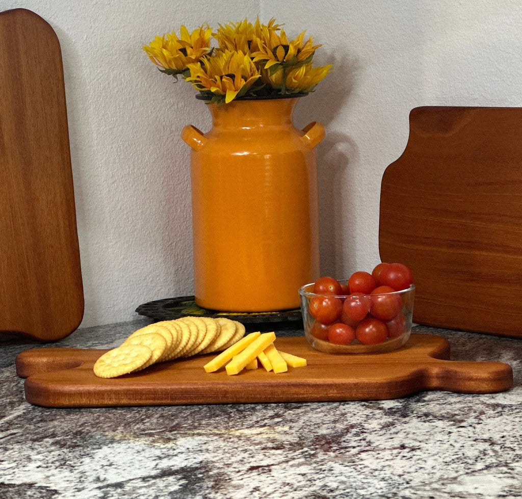 Mahogany red hardwood jigsaw puzzle shaped charcuterie board with cherry tomato, cheese and crackers displayed in front of an orange milk can vase with sunflowers and other cheese boards
