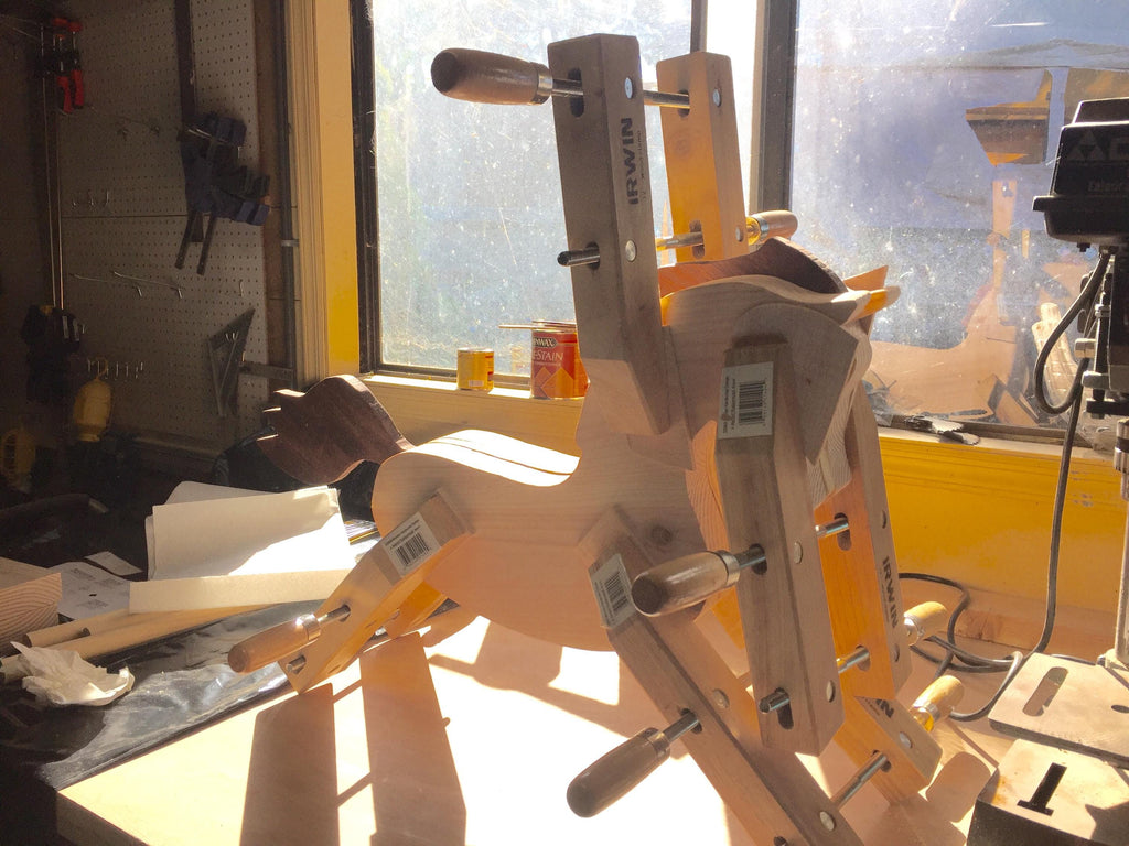 Assembled custom made antique style wooden rocking horse with wood clamps holding pieces in place to dry