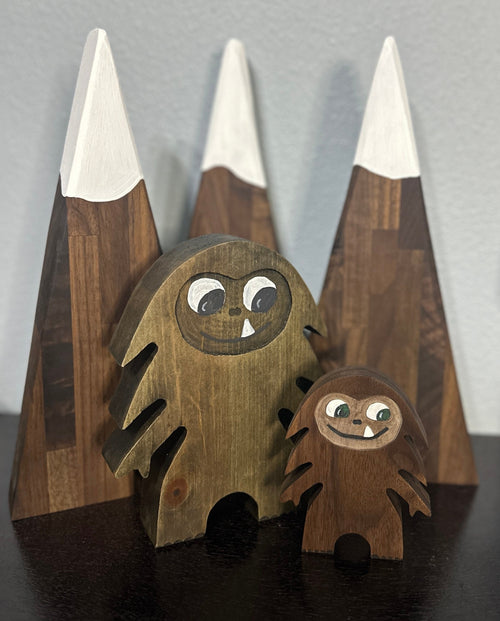 Hardwood Large and small Bigfoot in walnut with smiling one-tooth mouth, background of 3 dark triangle mountains with white painted snowcaps