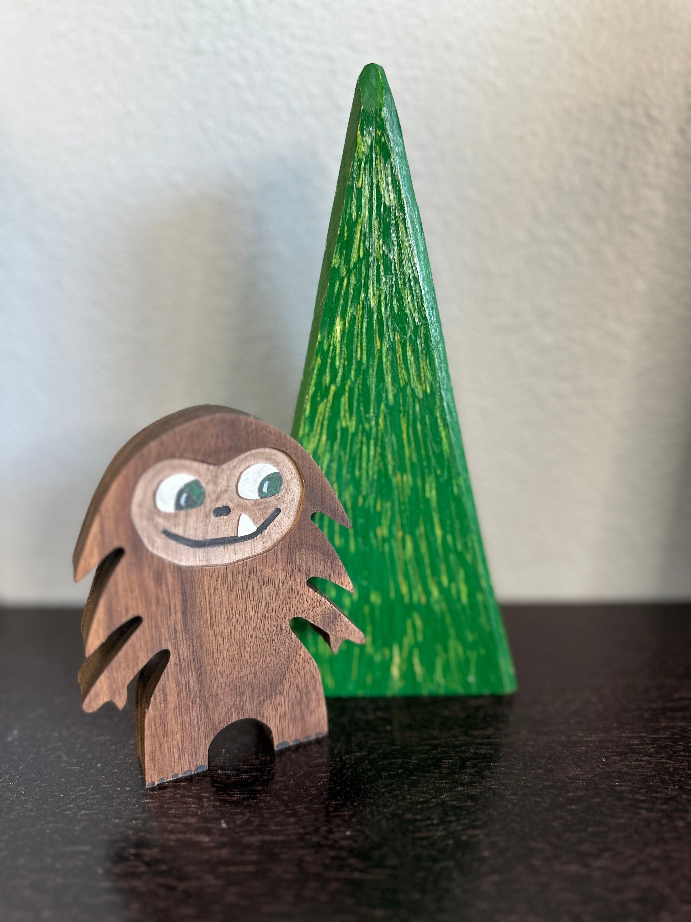 Hardwood small Bigfoot in walnut with smiling one-tooth mouth, background of  green triangle tree