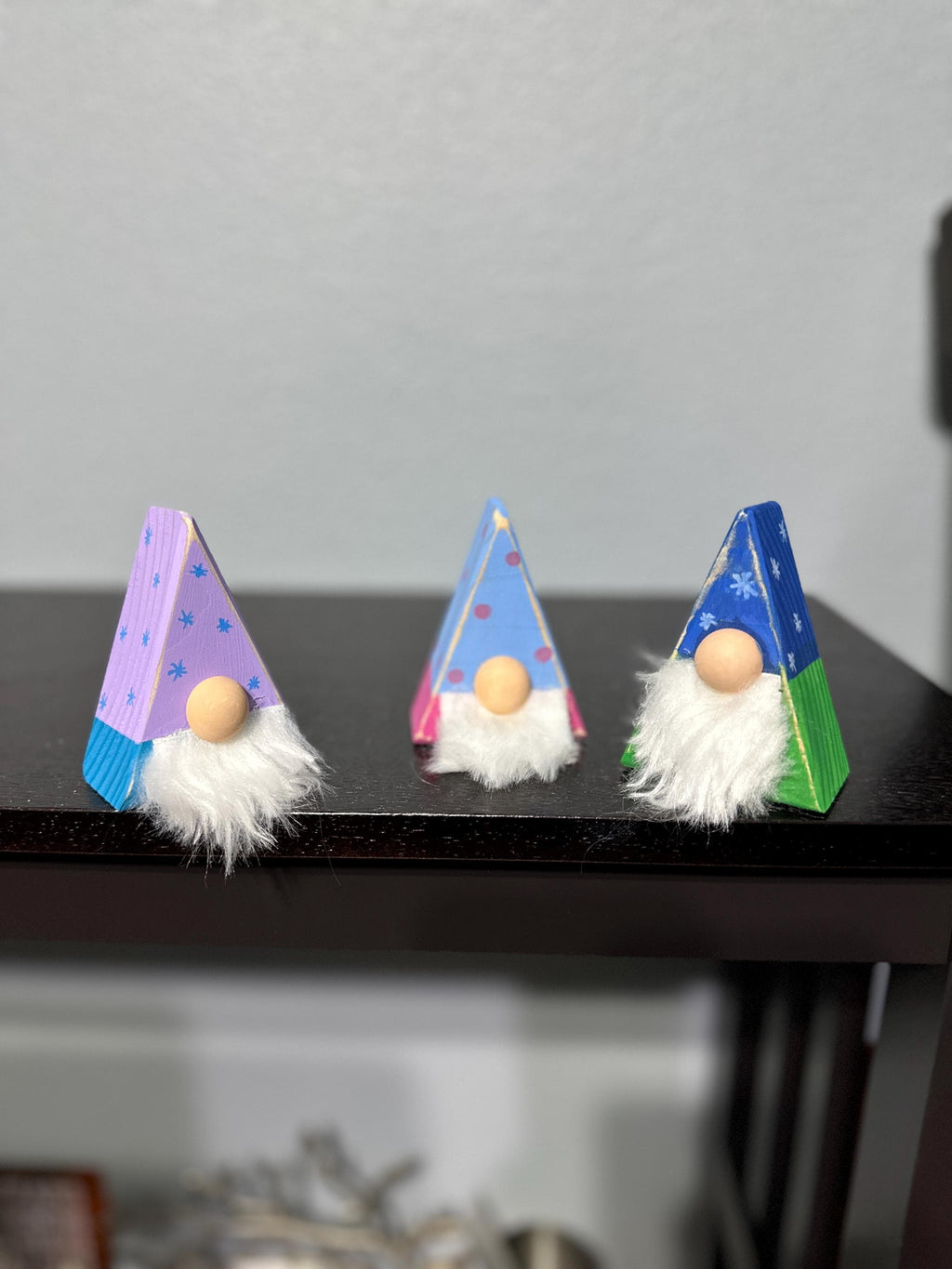 3 triangle gnomes with differently patterned painted antiqued hats sitting on a shelf