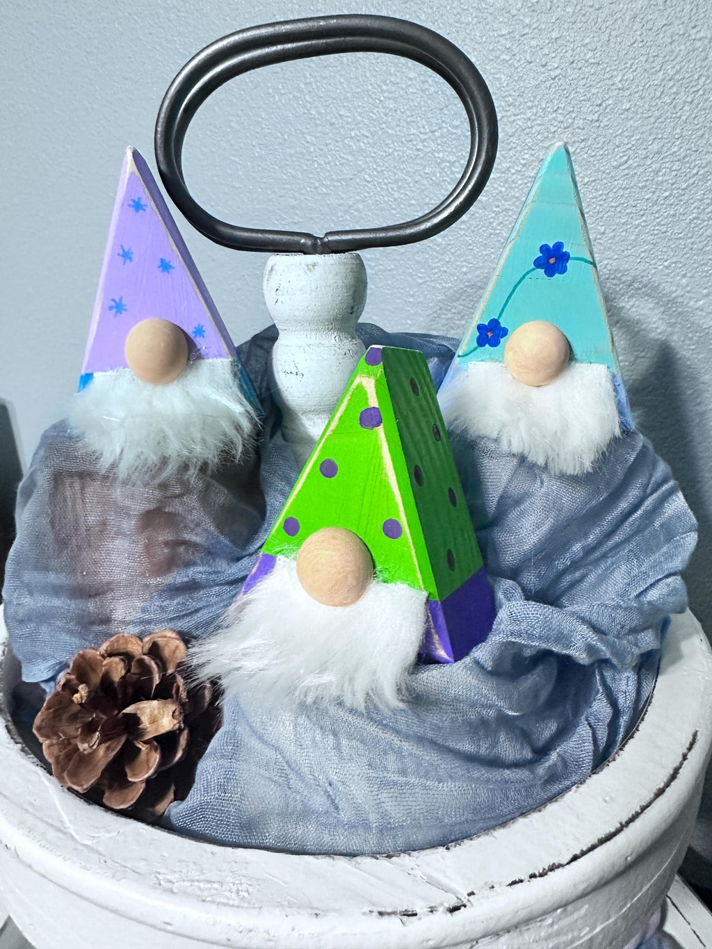 3 triangle gnomes with painted antiqued hats sitting on a tiered tray display with a pinecone