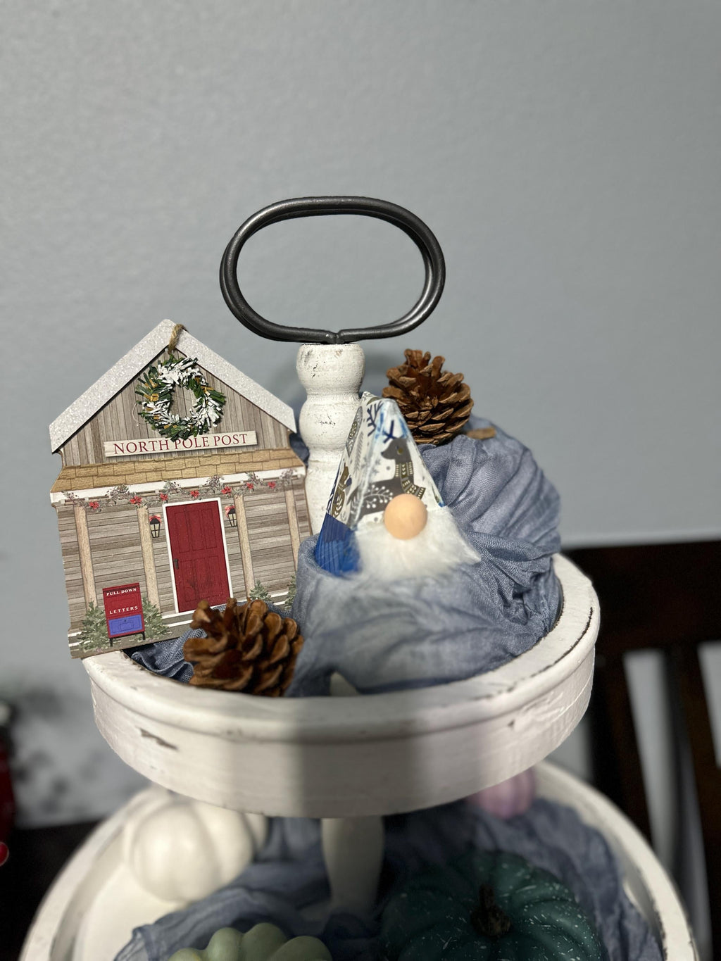 triangle gnome with Christmas antiqued hat sitting on a tiered tray holiday display with a pinecone & Northpole post office picture