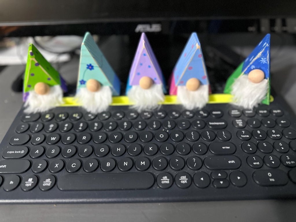 5 triangle gnomes with differently painted antiqued hats sitting on computer keyboard