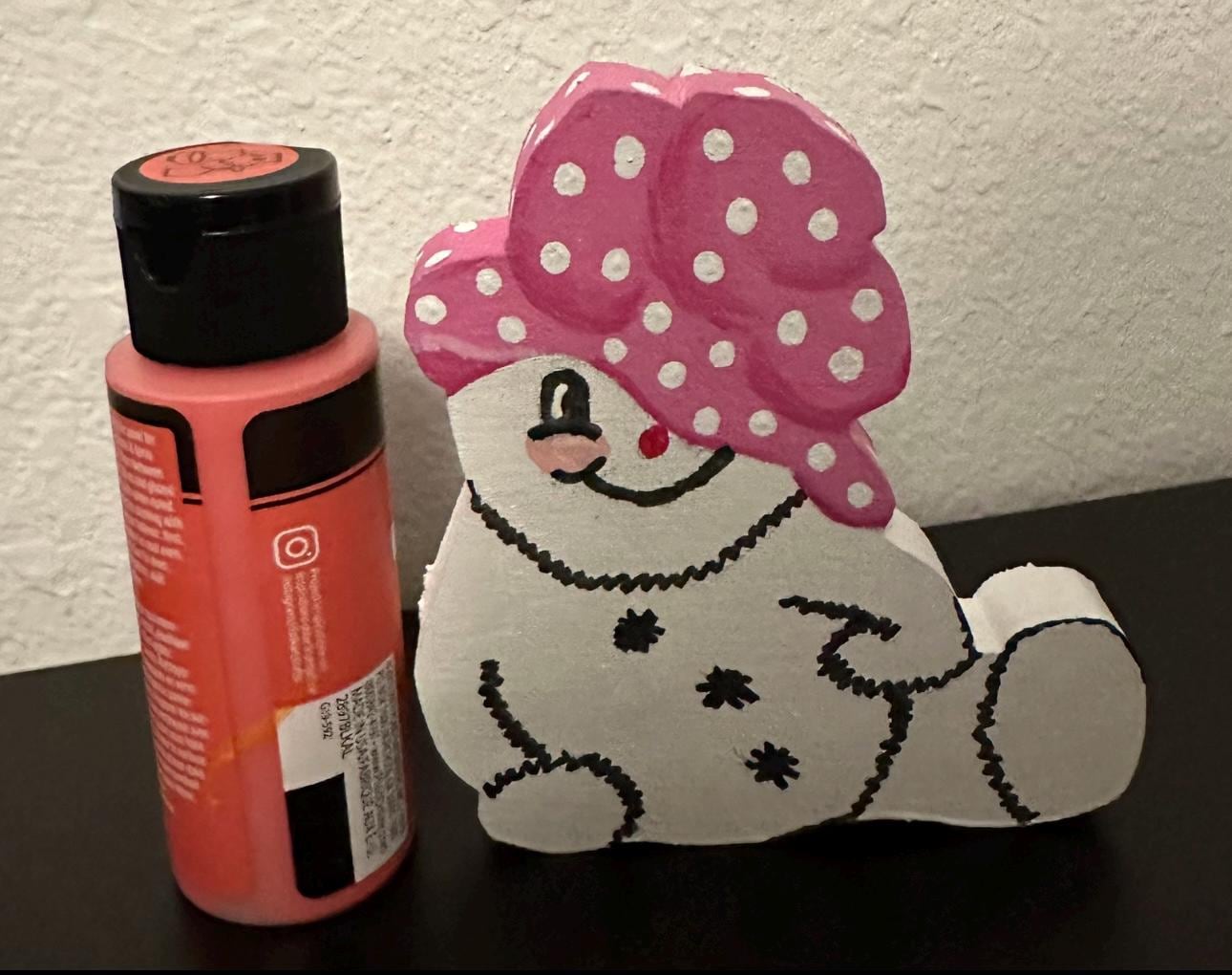 Wood painted snow woman shelf sitter with pink painted cap sitting next to 2oz paint bottle