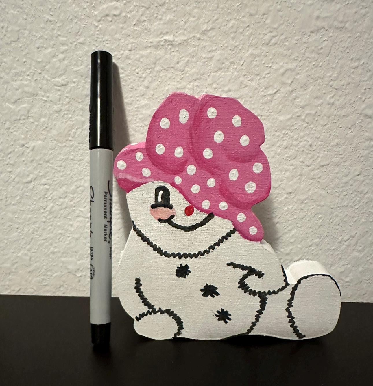 Wood painted snow woman shelf sitter with pink painted cap sitting next sharpie pen for size comparison