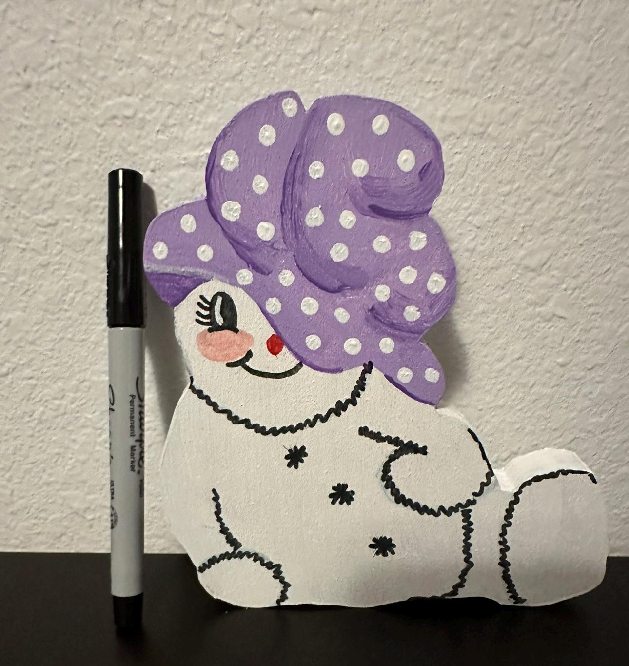 Wood painted snow woman shelf sitter with purple painted cap sitting next sharpie pen for size comparison
